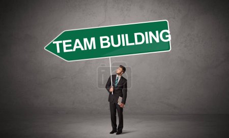 Photo for Young business person in casual holding road sign with TEAM BUILDING inscription, new business direction concept - Royalty Free Image