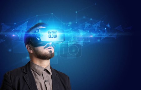 Businessman looking through Virtual Reality glasses with HYBRID CLOUD inscription, cyber security concept