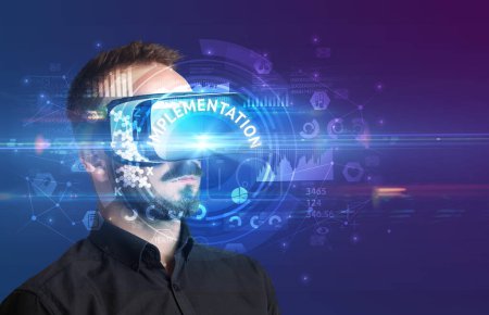 Homme d'affaires regardant à travers des lunettes de réalité virtuelle avec inscription IMPLEMENTATION, concept technologique innovant
