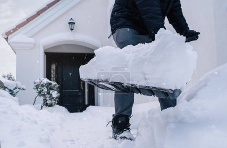 Primer plano de manos masculinas paleando nieve frente a la casa