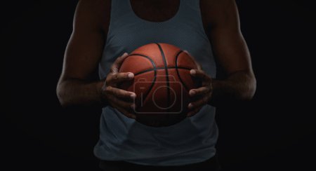 Téléchargez les photos : Gros plan de ballon de basket dans les mains des athlètes, isolé sur fond noir avec espace de copie - en image libre de droit