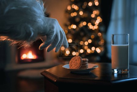 Téléchargez les photos : Le Père Noël reeaching pour le verre de lait et les biscuits à la chambre de Noël confortable - en image libre de droit