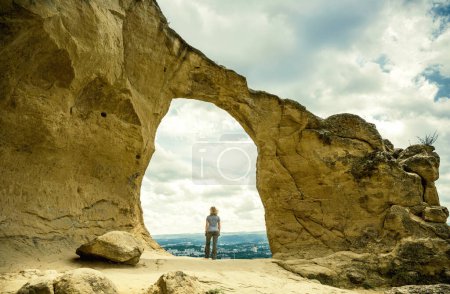 Hiker stands at Mountain Ring top, Kislovodsk, Stavropol Krai, Russia. Scenic view of person, peak and sky. Landscape with bizarre rock in summer. Theme of nature, travel people, hike and Kislovodsk.