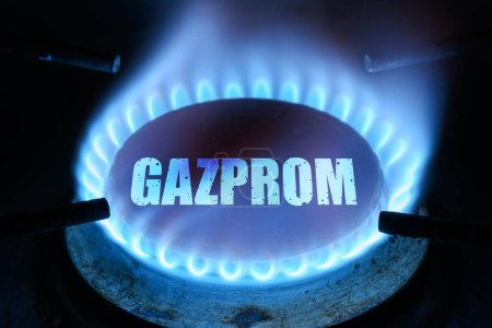 Gas burns in dark at home, blue fire flame and name Gazprom on stove ring burner. Concept of natural pipeline gas cost, warmth, energy crisis, economy, Russian Gazprom supply and Nord Stream 2.