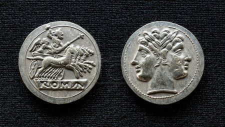 Téléchargez les photos : Ancient Roman coin showing Jupiter on horses and god Janus, 225-214 BC. Old rare money, silver didrachm isolated on dark background, macro. Concept of Rome, valuable coin, civilization and history. - en image libre de droit