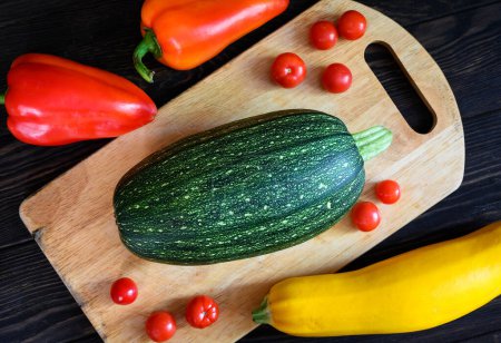 Photo for Vegetable marrow and sweet pepper on wooden table, flat lay. Top view of fresh zucchini and tomatoes on cutting board, set of organic food. Concept of squash, cooking, healthy eating, nature. - Royalty Free Image
