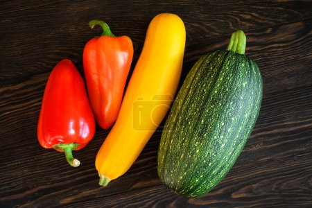 Photo for Vegetable marrow and sweet pepper on dark wooden table, flat lay. Top view of fresh zucchini on vintage planks, set of organic food. Concept of squash, cooking, healthy eating, nature. - Royalty Free Image