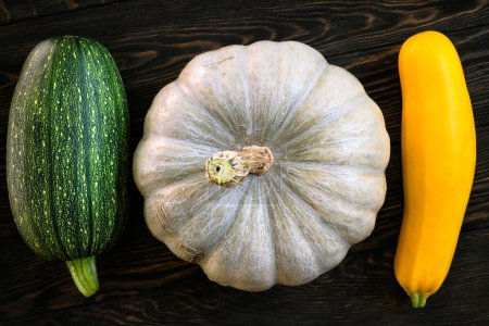 Photo for Pumpkin and vegetable marrow on dark wooden table, flat lay. Top view of fresh zucchini on vintage planks, set of organic food. Concept of squash, cooking, healthy eating, nature. - Royalty Free Image
