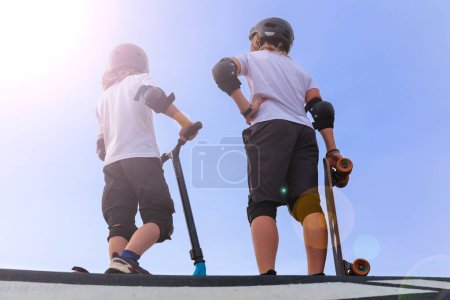 Foto de Dos niños con scooter y monopatín en skatepark- jóvenes activos - Imagen libre de derechos