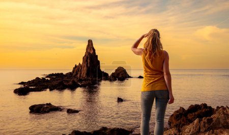 Foto de Woman enjoying beautiful sunset at the sea with rocks - Imagen libre de derechos