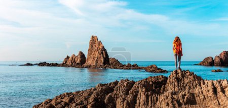 Téléchargez les photos : Woman stands on rock peak looking at the sea ( cabo de gata, Andalusia in Spain) - en image libre de droit