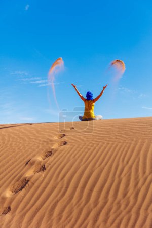 Foto de Mujer con turbante azul en el desierto del Sahara arrojando arena sobre el cielo azul Marruecos - Imagen libre de derechos