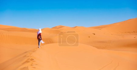 Foto de Joven hermosa mujer caucásica posando con textiles blancos volando en el desierto del sahara en Marruecos - Imagen libre de derechos