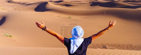 Téléchargez les photos : Homme portant un turban blanc dans le désert du Sahara - tourisme au Maroc - en image libre de droit
