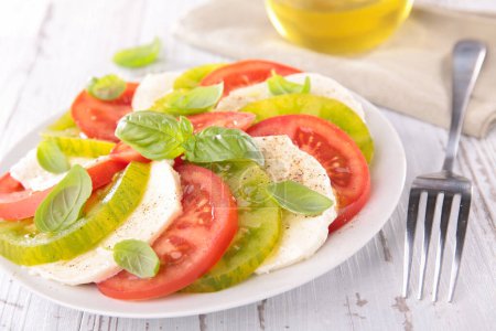 Photo for Tomato salad- slices of green and red tomato with slice of mozzarella and basil- Caprese salad - Royalty Free Image