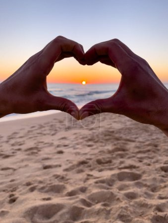 Téléchargez les photos : Coucher de soleil dans les mains du cœur sur la plage - en image libre de droit