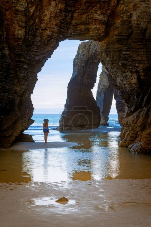 Foto de Playa las catedrales, turismo turístico en Galicia, Mujer, arco natural y playa- España - Imagen libre de derechos