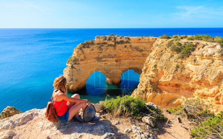 Foto de Turista mujer disfrutando de hermosa cueva o formación de roca en forma de corazón en el océano atlántico- Costa del Algarve en Portugal - Imagen libre de derechos