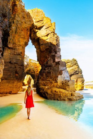 Photo for Beautiful woman with red dress walking on famous cathedral beach in Galicia, Spain - Royalty Free Image