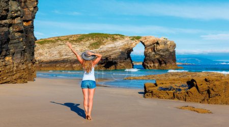 Téléchargez les photos : Femme aux bras levés profitant de l'océan Atlantique et de la formation rocheuse- plage cathédrale avec arche et cave- Galice, Espagne - en image libre de droit