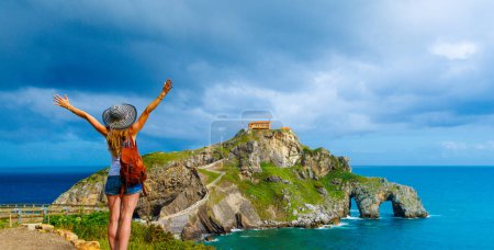 Téléchargez les photos : Heureuse femme avec les bras levés sur l'île Gaztelugatxe sur la côte de la baie de Gascogne Pays basque, près de bilbao et Santander- Espagne - en image libre de droit