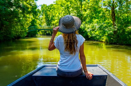 Rückansicht einer Frau mit Hut auf einem Boot mit Blick auf den Fluss - Marais poitevin in Frankreich