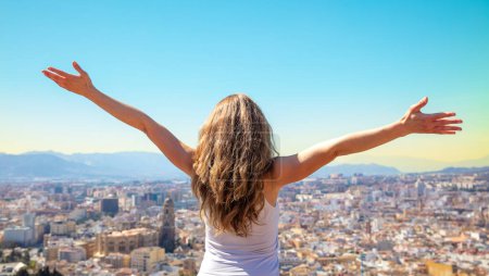 Téléchargez les photos : Heureuse femme libre avec les bras levés admirant skyling de la ville de Malaga skyline de la ville avec les bras tendus levés dans le ciel succès, Voyage, concept de vie active - en image libre de droit