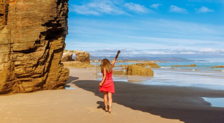 Téléchargez les photos : Femme avec robe rouge profitant de la belle plage et la côte avec des archées- Cathédrales plage, Galice, Espagne - en image libre de droit