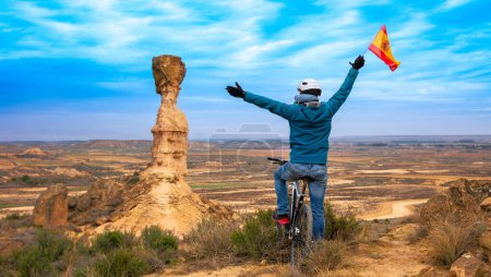 Photo for Man in bike holding spanish flag- Aragon viewpoint in countryside,  Monegros desert - Royalty Free Image