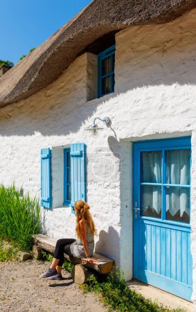 Téléchargez les photos : Femme assise sur banc, maison de breton traditionnelle avec toit de chaume- Bretagne, France - en image libre de droit