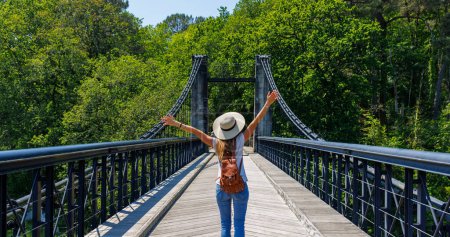 Foto de Mujer feliz turista con los brazos levantados en puente colgante sobre el río en el bosque-Europa - Imagen libre de derechos