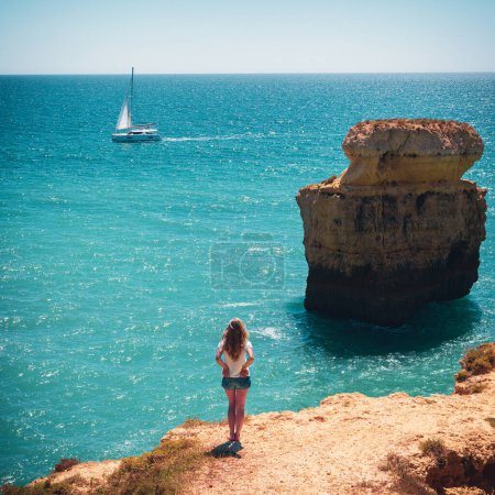 Foto de Destino de viaje, concepto de vacaciones de verano- mujer mirando barco en el océano atlántico en Portugal- Costa del Algarve - Imagen libre de derechos