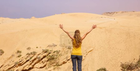 Foto de Mujer con brazos abiertos disfrutando de dunas de arena en Marruecos - Imagen libre de derechos