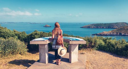 Photo for Woman tourist standing on orientation table looking at panoramic view of atlantic ocean in Brittany, France - Royalty Free Image
