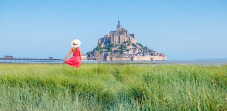 Foto de Mujer turista con vestido rojo mirando el Mont Saint Michel- vacaciones, destino de viaje, turismo turístico en Normandía, Francia - Imagen libre de derechos