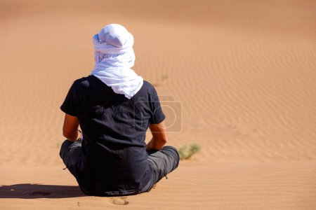 Foto de Hombre caucásico con turbante blanco sentado y mirando el desierto - Imagen libre de derechos