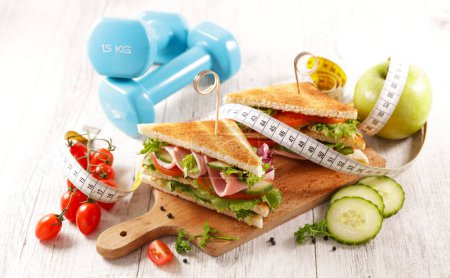 Foto de Dieta concepto de alimentos- sándwich con pan tostado y verduras, mancuerna y medidor - Imagen libre de derechos