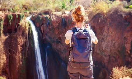 Téléchargez les photos : Vue arrière de la femme touriste prenant une photo de la cascade d'Ouzoud au Maroc - en image libre de droit
