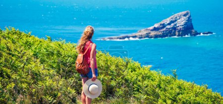Foto de Mujer con mochila y sombrero mirando a la isla en el océano atlántico- Aventura, viajes, concepto de vacaciones - Imagen libre de derechos