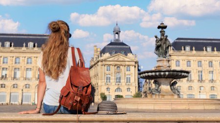 Mujer estudiante o turista sentada en el banco mirando la plaza Bourse en Burdeos-Francia