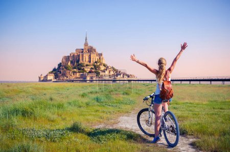 Foto de Mujer feliz turista en bicicleta disfrutando de la vista del Mont Saint Michel al amanecer Normandía en Francia - Imagen libre de derechos