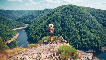 Foto de Mujer con sombrero y mochila de pie en la cima de la montaña disfrutando de una hermosa vista (Dordogne en Francia) - Aventura, viajes, libertad o concepto exitoso - Imagen libre de derechos
