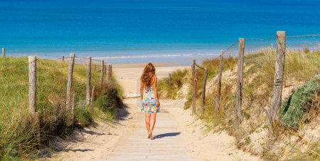 Téléchargez les photos : Femme marchant sur un chemin en bois jusqu'à la plage - en image libre de droit