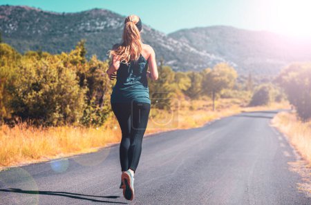 Foto de Mujer corriendo al amanecer en la carretera en el país, deporte, concepto de mujer activa - Imagen libre de derechos
