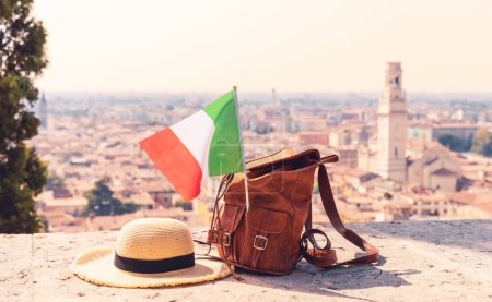 Sonnenhut, Tasche und italienische Flagge mit italienischer Stadt im Hintergrund (Verona, Venetien) - Reise, Urlaub, Tourtourismus in Italien Konzept