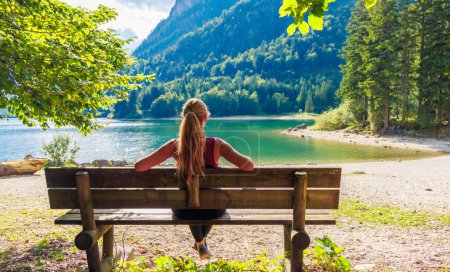 Téléchargez les photos : Femme assise sur un banc regardant spectaculaire lac émeraude en montagne- Voyage, détente, concept de vacances d'été - en image libre de droit