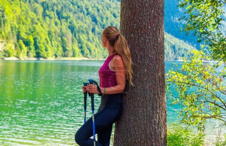 Foto de Mujer deportiva con bastón mirando hermoso lago en la montaña- Deporte, viajes, concepto de bienestar (Lago del Predil en Italia) - Imagen libre de derechos