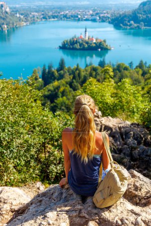 Foto de Joven turista sentada en la roca mirando la vista panorámica sobre el lago Bled-turismo turístico, viajes, vacaciones en Eslovenia-Europa - Imagen libre de derechos