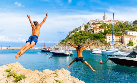 Téléchargez les photos : Heureuse famille sautant du rocher dans la mer (Croatie, Europe) - en image libre de droit