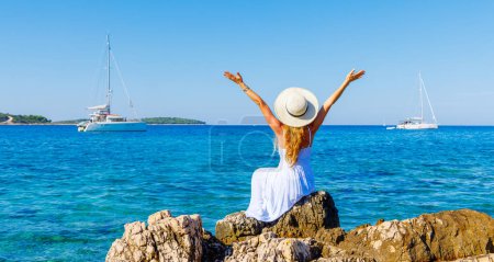 Foto de Destino de viaje, vacaciones de verano, concepto de crucero - Mujer feliz en vestido blanco con los brazos abiertos disfrutando del mar y yate de vela (Dalmacia, Croacia) - Imagen libre de derechos